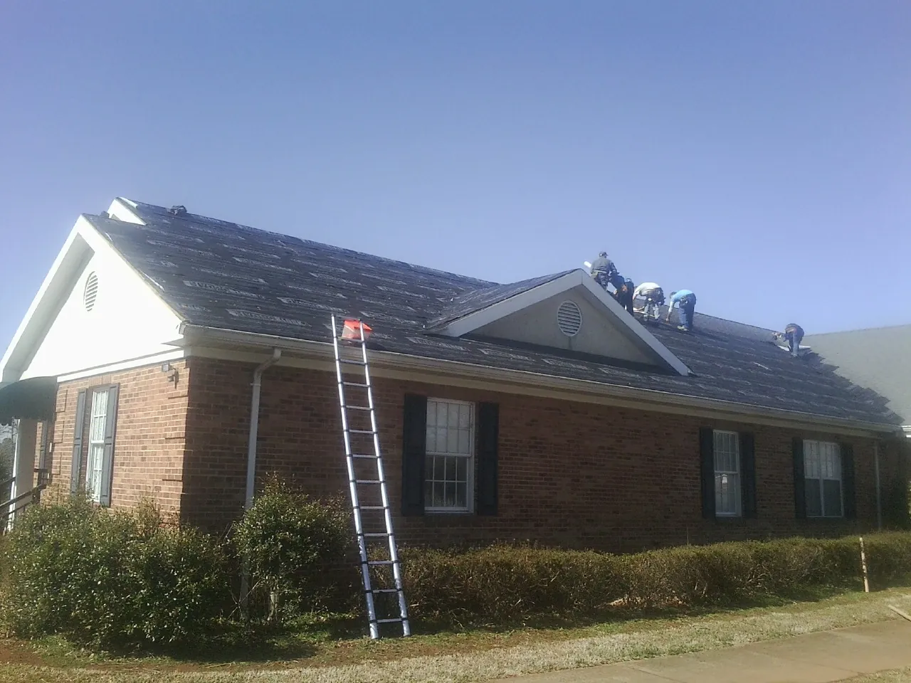 Crew tearing shingles off a brick ranch roof with a ladder set — Emergency Roof Repair work by our crew in Kennett Square