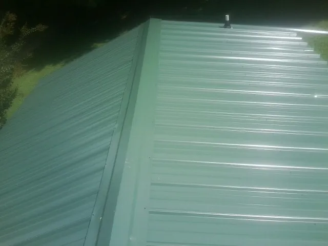 New green metal panels meeting at the ridge of a roof — Flat Roof Repair work by our crew in Kennett Square