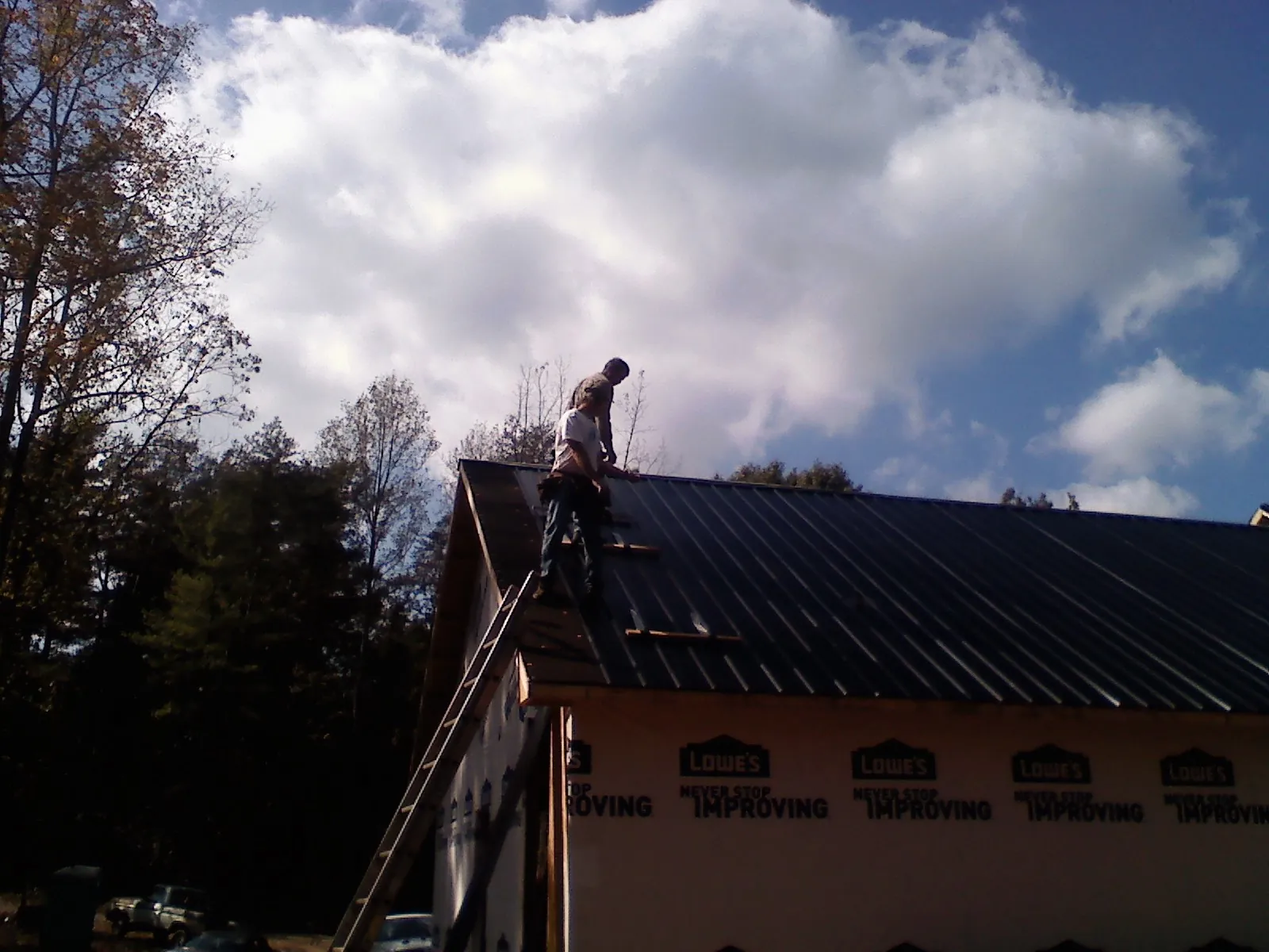 Roofer fastening dark metal panels high against a cloudy sky, from a Roof Inspection job in Kennett Square