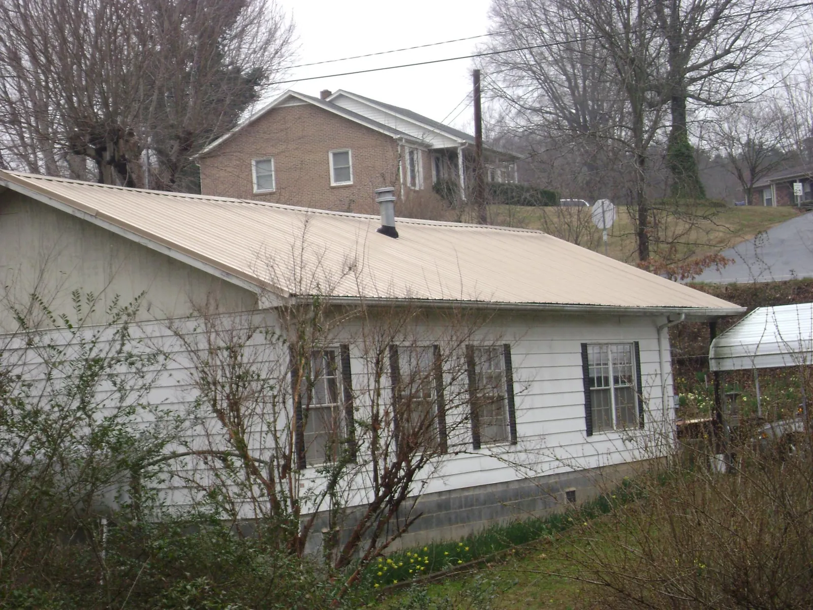 Tan metal roof on a white sided house set into a hillside — Commercial Roofing by Roofing Brothers in Kennett Square